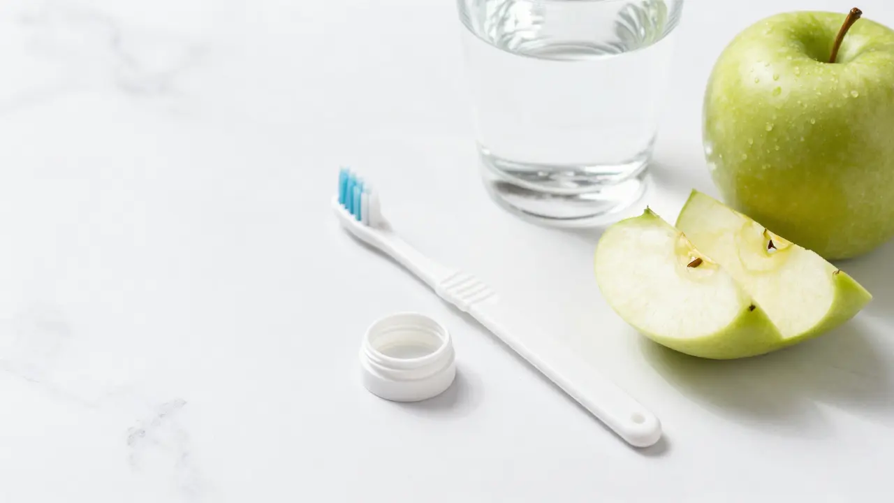 Sada pomůcek pro hygienu zubů s keramickými rovnátky a zdravé jablko.