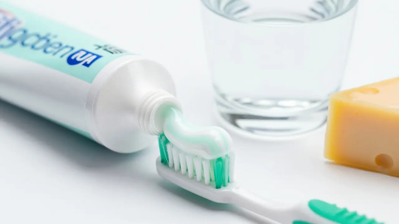 Zubní pasta na kartáčku vedle vody a sýra pro prevenci zubního kazu